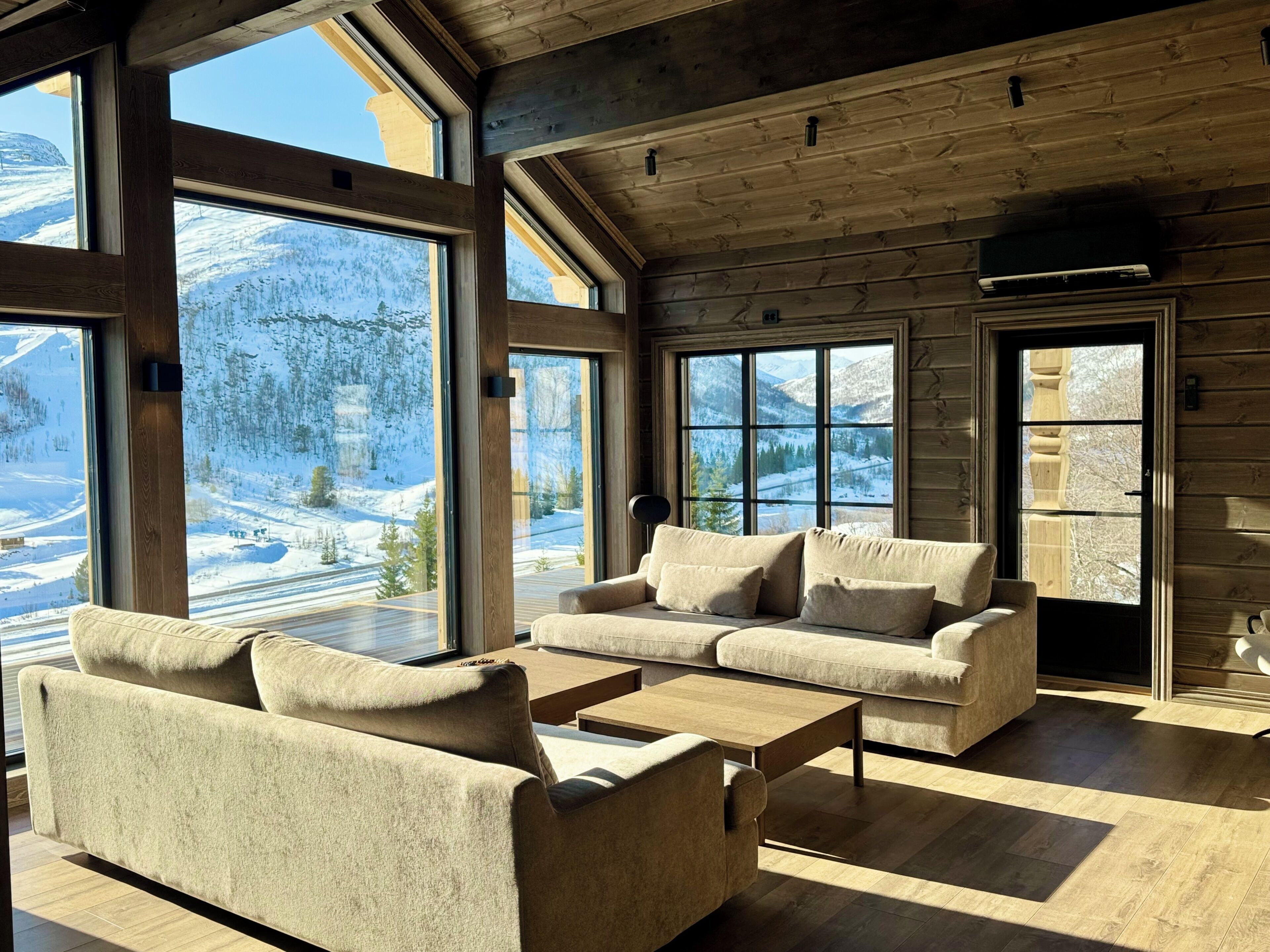 Ein gemütliches Blockhaus-Interieur mit großen Fenstern und Blick auf die Berge, einer Couch und einem Couchtisch.