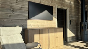 Een modern interieur met een houten wand, een flatscreen televisie boven een kast, en een comfortabele stoel.