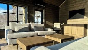 Een gezellig cabin interieur met een hoekbank, een houten salontafel en een aan de muur bevestigde televisie.