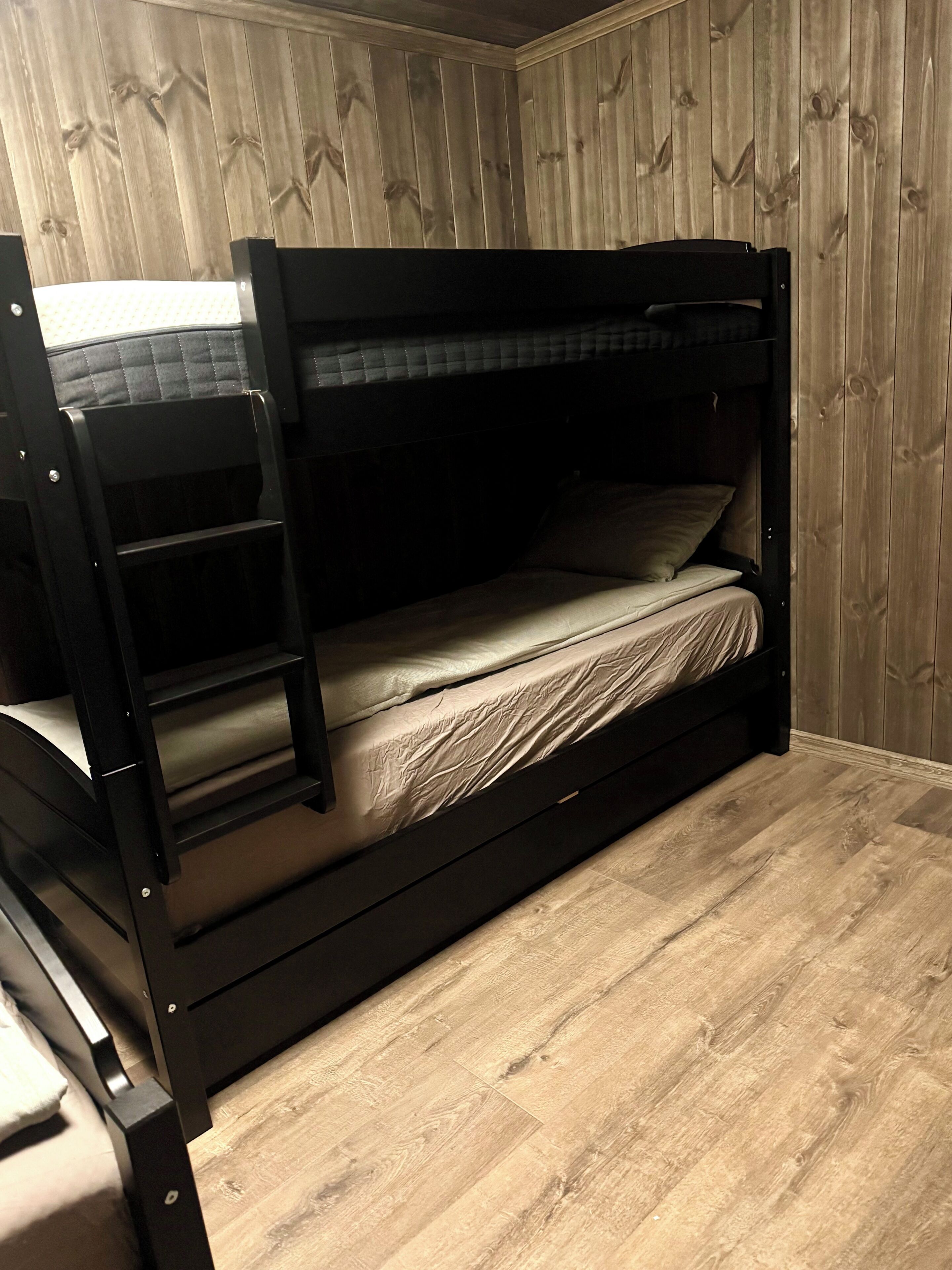 A bunk bed with a ladder, wooden walls, and a wooden floor.