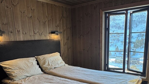 Een tweepersoonsbed met hoofdeinde, een raam met uitzicht op een besneeerd landschap en een houten plafond.