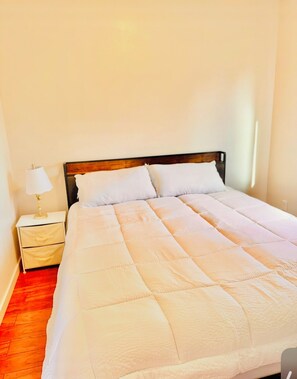 Una cama individual con cabecera de madera en una habitación con pared blanca y suelo de madera.