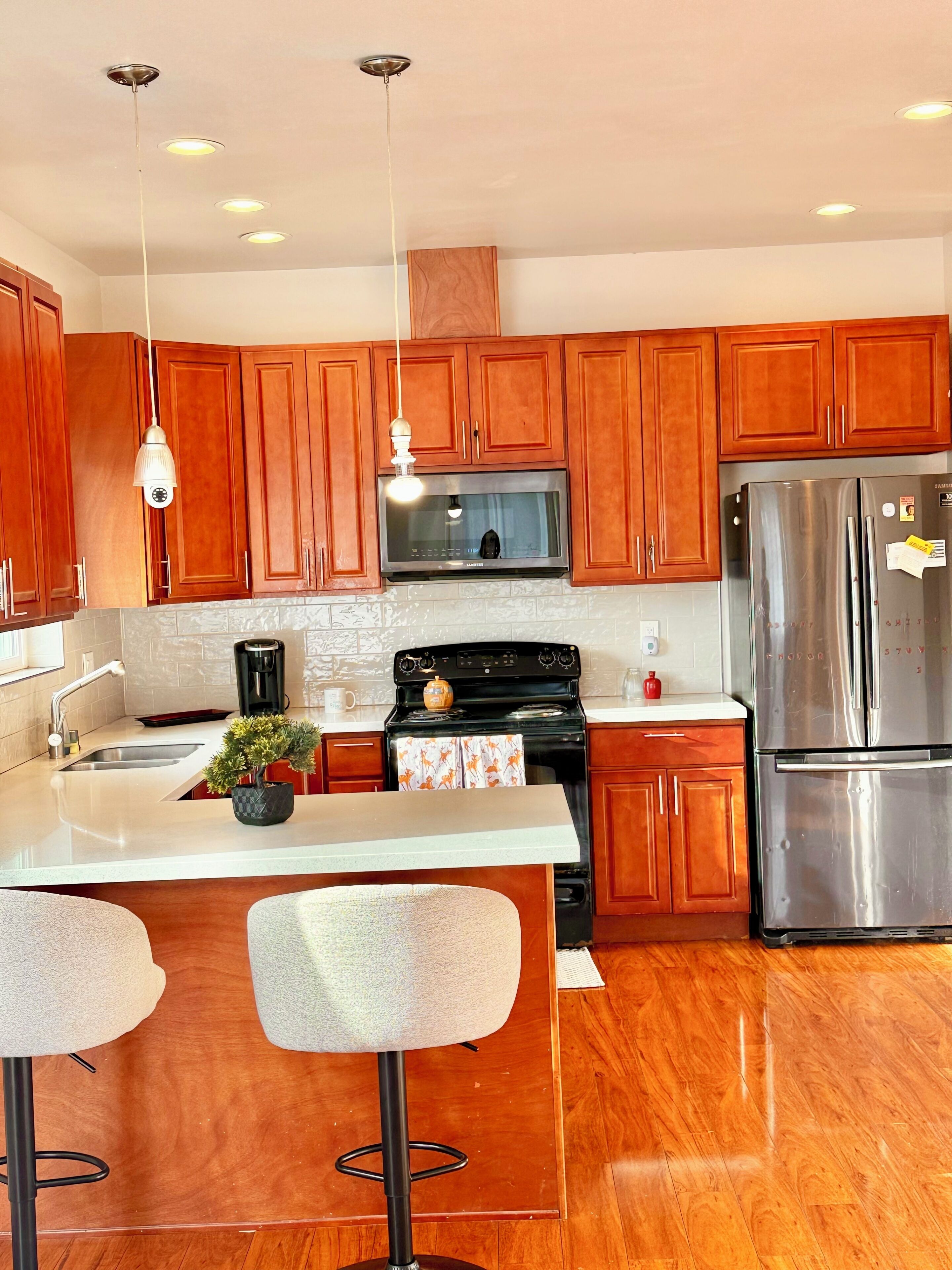 A modern kitchen with wooden cabinets, stainless steel appliances, a central island with bar stools, and pendant lighting.