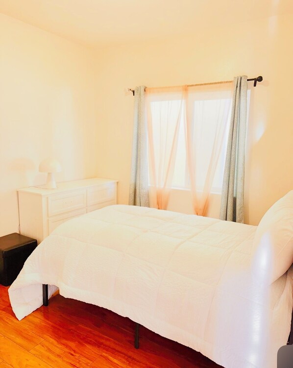 A bedroom with a bed, a nightstand, a dresser, and a window with curtains.