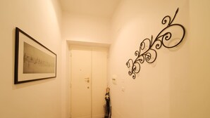 Ein Flur mit einem gerahmten Bild links, einer Tür am Ende und einem dekorativen Metallkunstwerk an der rechten Wand.