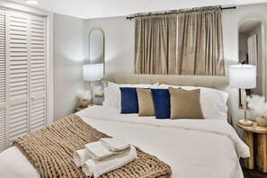 A neatly made bed with a beige blanket, a headboard, and a bedside table with a lamp and a vase.