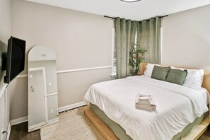 A bedroom with a bed, a television, a mirror, and a window with curtains. - Bright & Cozy Homewood 3 Bed with Arcade Game! (Homewood)