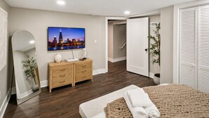 Une chambre à coucher comprenant un lit, une commode, un miroir, un tableau représentant un paysage urbain et un placard.
