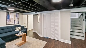Un intérieur moderne avec un canapé bleu foncé, une table basse en bois, un tapis blanc, une grande peinture abstraite et un ensemble d’armoires blanches à persiennes.