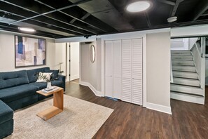 A modern interior with a dark blue sofa, a wooden coffee table, a white rug, a large abstract painting, and a set of white louvered closets.