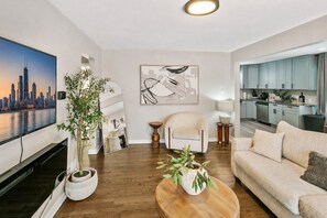 A modern living room with a flat-screen TV, a sofa, a coffee table, and a painting on the wall. - Bright & Cozy Homewood 3 Bed with Arcade Game! (Homewood)