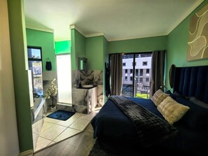 Ein modernes Schlafzimmer mit einem großen Bett, einem Badezimmer mit Waschtisch und einem Balkon mit Blick auf Gebäude.
