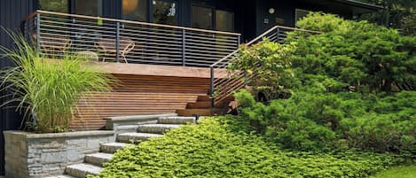 A modern building with a large glass facade, a wooden deck, and a well-maintained garden.