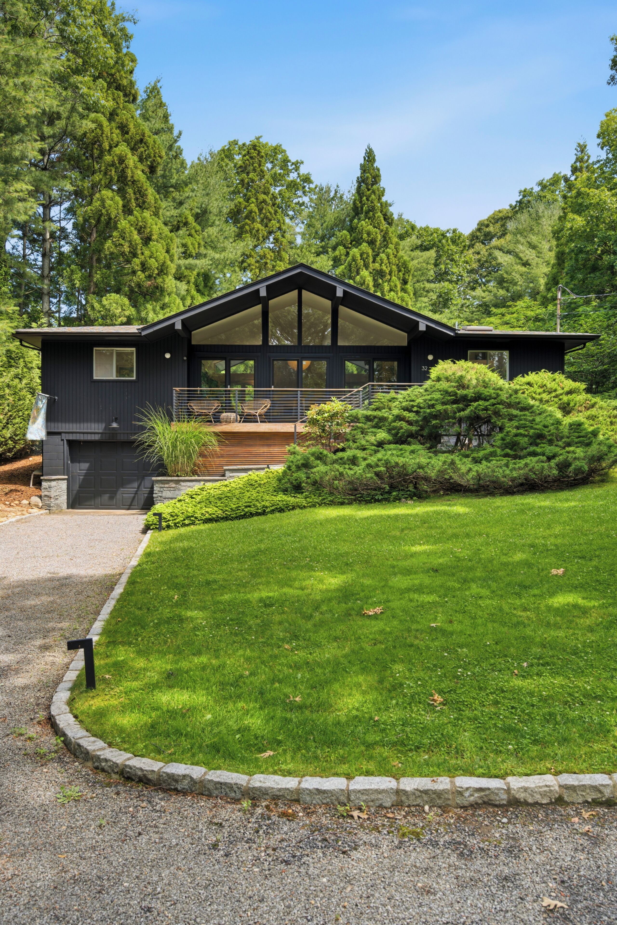 A modern two-story house with a covered porch, surrounded by lush greenery and trees.