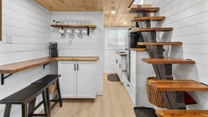 Una cucina compatta con mobili bianchi, mensole in legno e un piano cottura integrato.