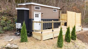 Un'abitazione mobile con un portico anteriore, un piccolo deposito annesso e un'area recintata con alberi sempreverdi.