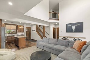 Ein geräumiges Wohnzimmer mit grauem Sofa, einem runden Couchtisch und einer Küche mit Holzausstattung und einer zentralen Kochinsel.