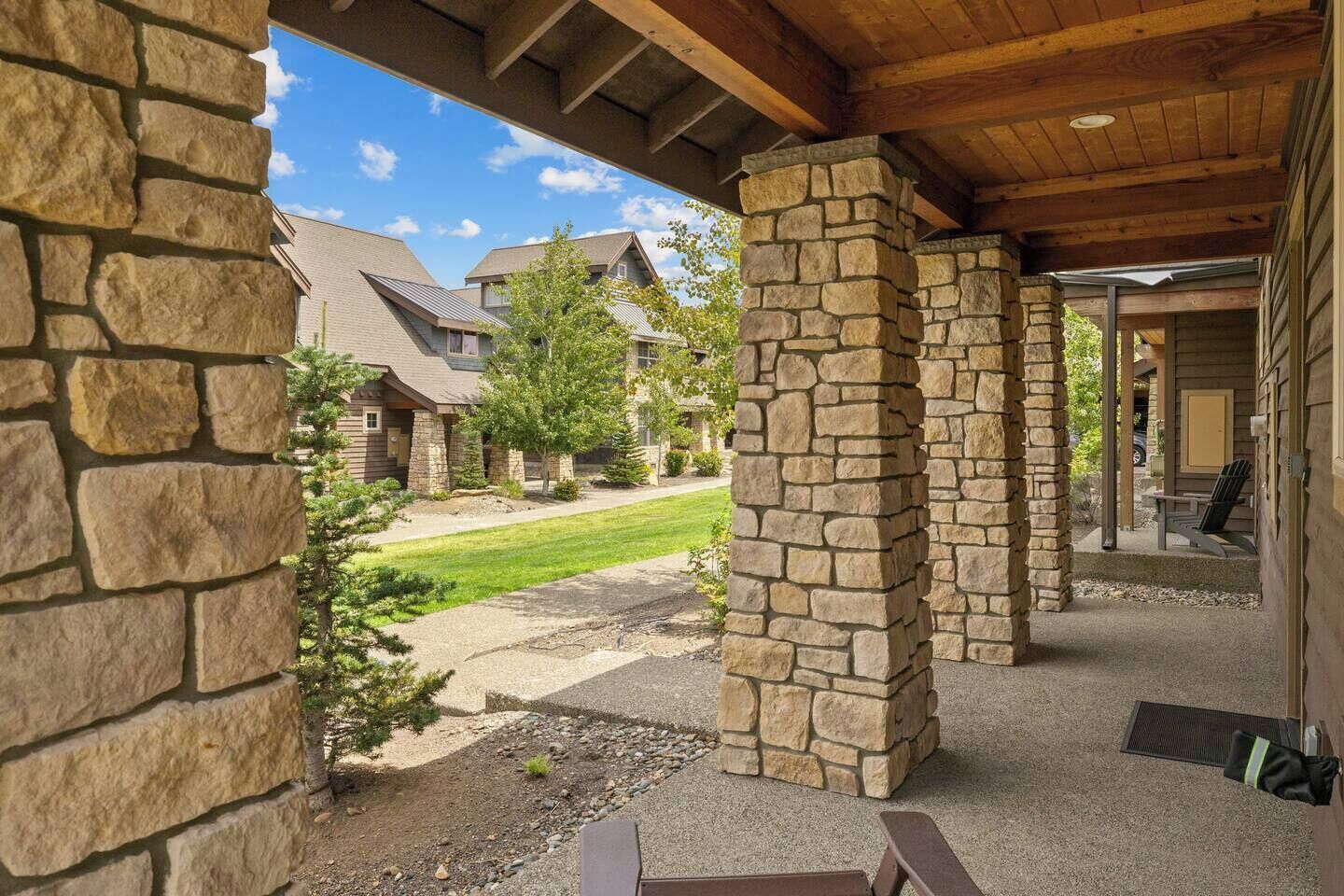 A covered outdoor area with stone pillars, a paved walkway, and a view of residential buildings in the background.