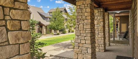 A covered outdoor area with stone pillars, a paved walkway, and a view of residential buildings in the background.