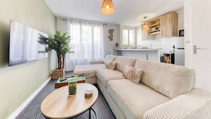 A modern living room with a sectional sofa, a round wooden coffee table, a potted plant, and a television mounted on the wall.