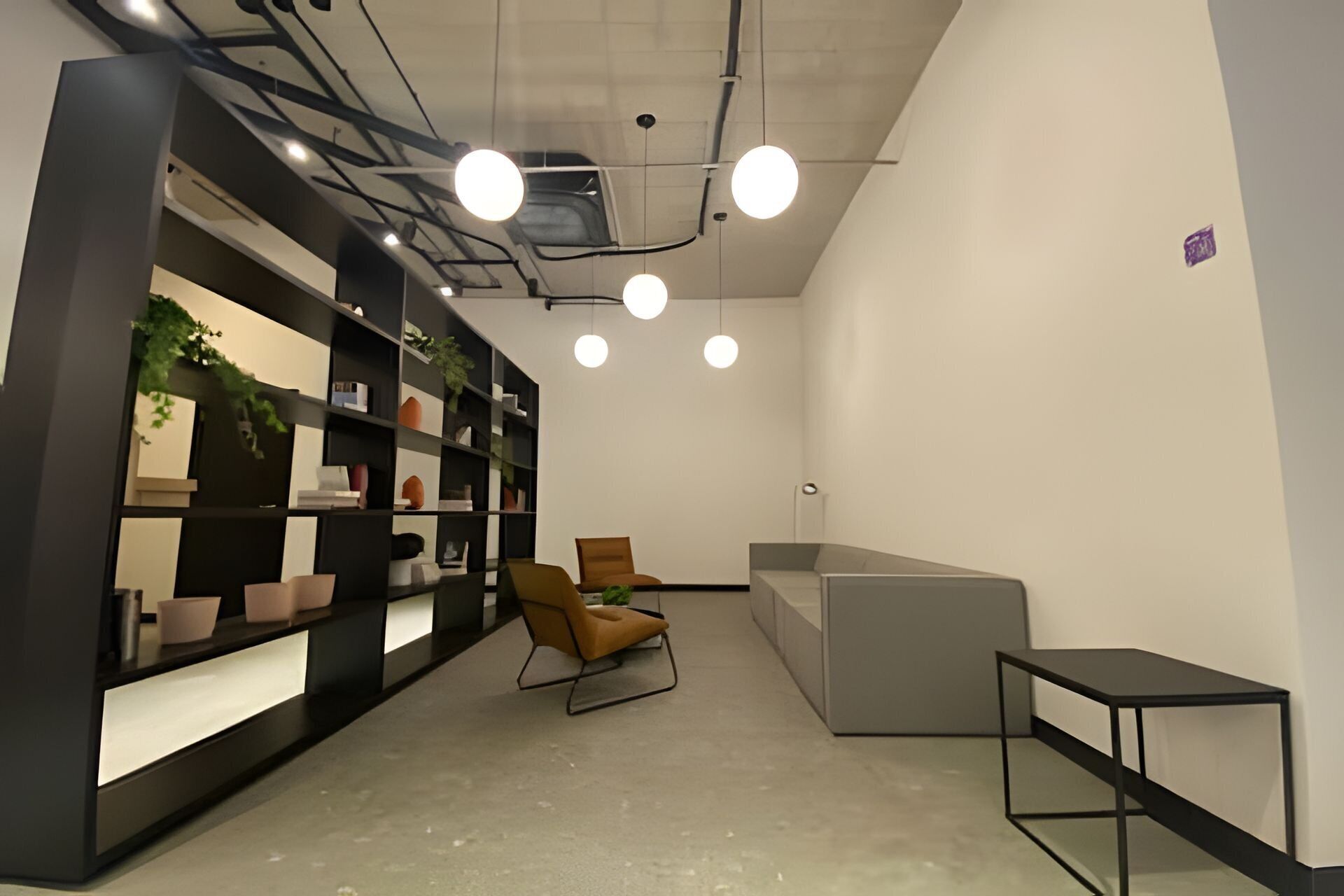 Un espace de bureau moderne avec une bibliothèque noire, un fauteuil marron, un canapé gris et une petite table noire.