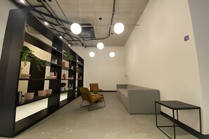 A modern office space with a black bookshelf, a brown chair, a grey sofa, and a small black table. - Studio novíssimo próximo à Paulista (São Paulo)