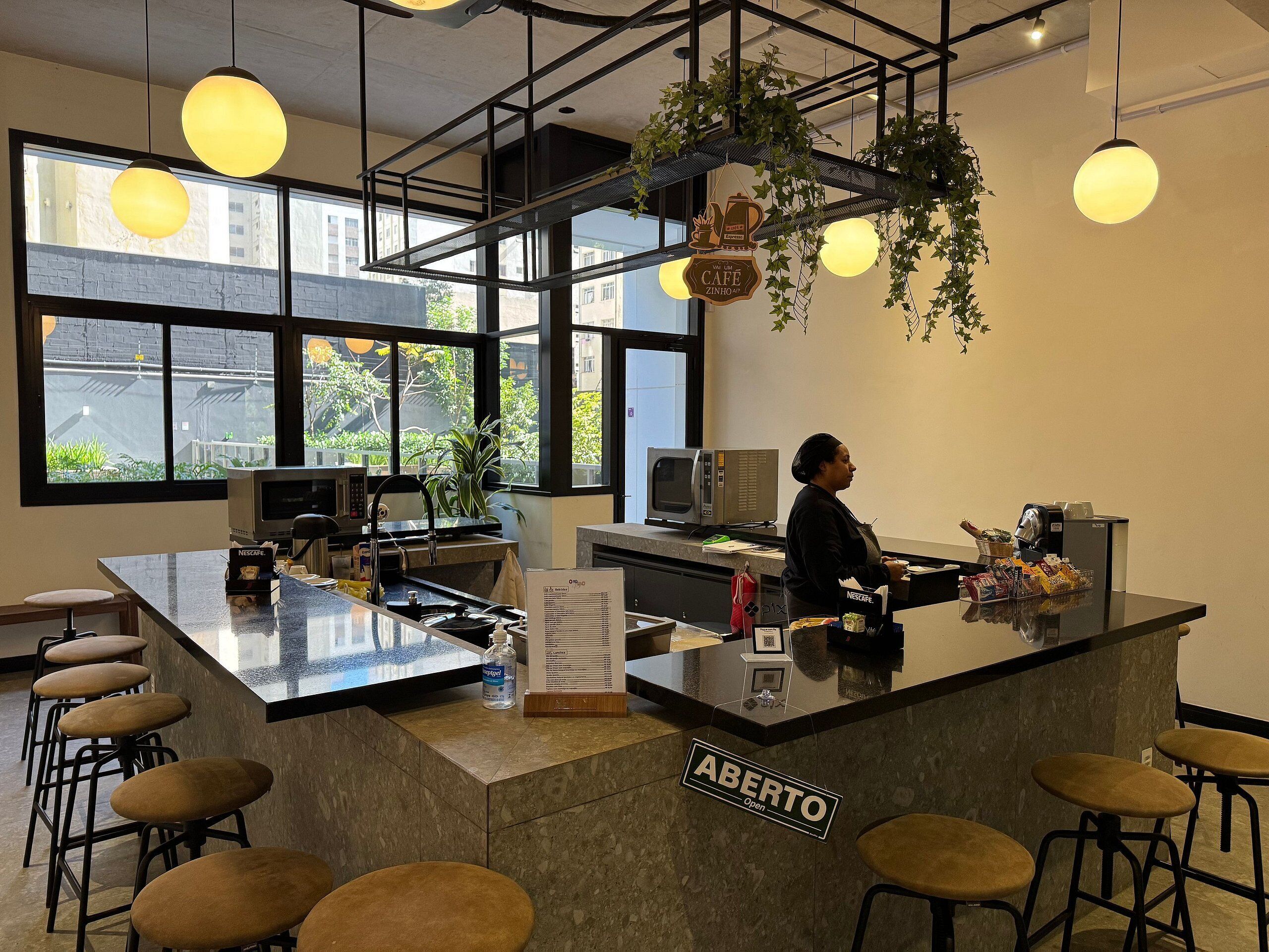 Interior de una cafetería moderna con barra, asientos y un letrero que indica que está abierta.