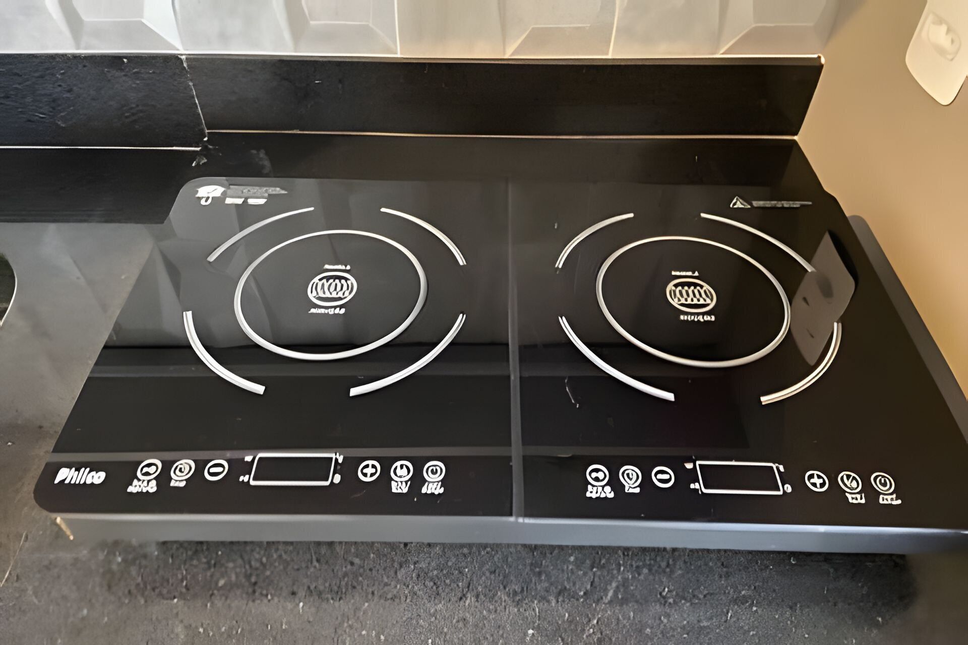 A black induction cooktop with two circular heating elements and a control panel with various icons.