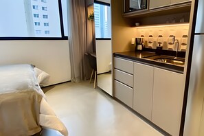 Une chambre d’hôtel compacte comprenant un coin cuisine, un lit et une fenêtre donnant sur un immeuble.
