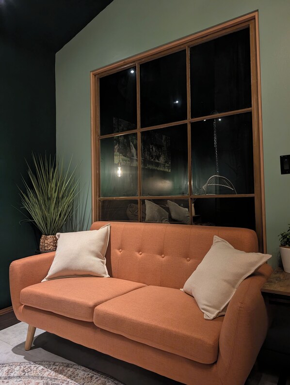A room with a large window, a sofa, and a potted plant.
