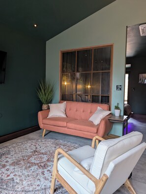 Un salon chaleureux avec une grande fenêtre, un canapé, un fauteuil et un tapis à motifs.