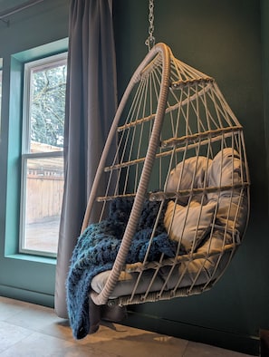 A hanging chair with a cushion and a blanket, positioned near a window with curtains.