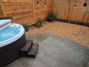 A hot tub with steps, a wooden fence, and string lights.