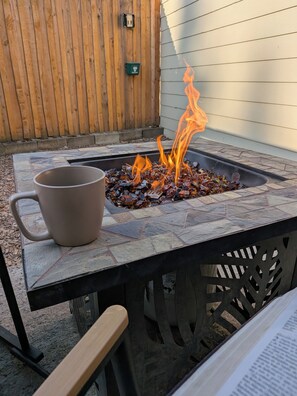Ein Lagerfeuer mit brennenden Holzscheiten, eine Kaffeetasse und ein Stuhl.