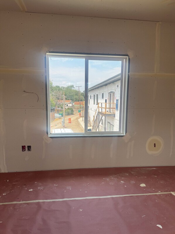 Une pièce dotée d’une grande fenêtre, dont les murs sont apparents et où l’on peut voir les matériaux de construction de l’extérieur.