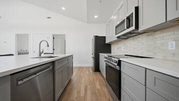 A modern kitchen with stainless steel appliances, white cabinetry, and a wooden floor.