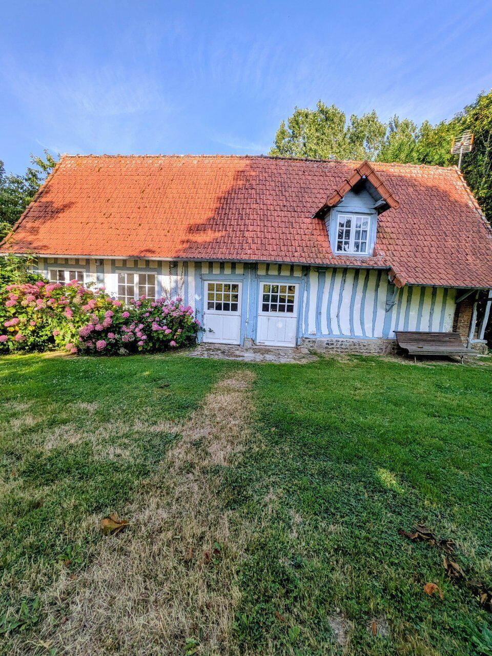 Een traditioneel huis met een rode pannendak, een wit en blauw gevel en een voordeur.