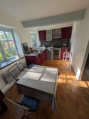 A kitchen with a dining table, a window with a view of greenery, and a tiled floor. - La Passée – House in Sainte-Marguerite-sur-Mer (Sainte-Marguerite-sur-Mer)