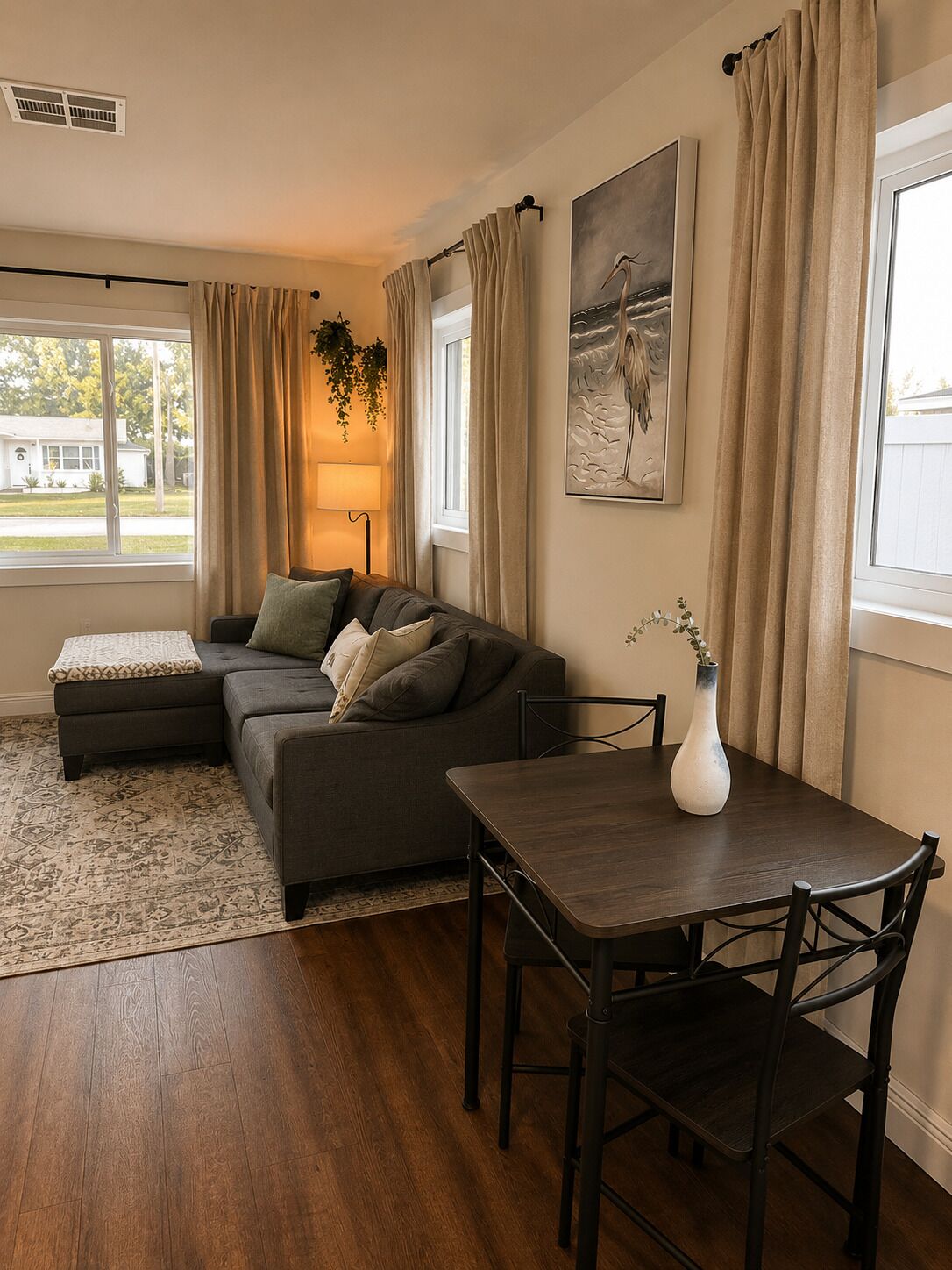 Ein Wohnzimmer mit Ecksofa, Esstisch mit Stühlen, einer Blumenvase, einer Lampe und einem Gemälde an der Wand.