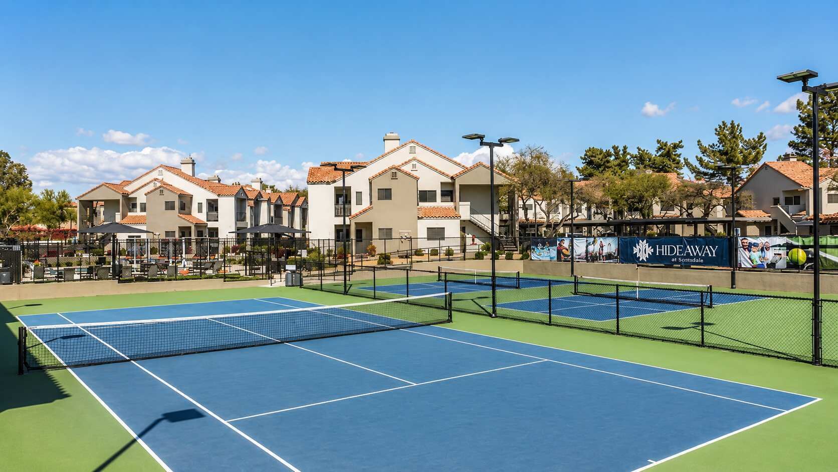 Un court de tennis avec un filet, entouré de bâtiments sur lesquels on peut lire l’inscription « Hideaway at Scranton ».