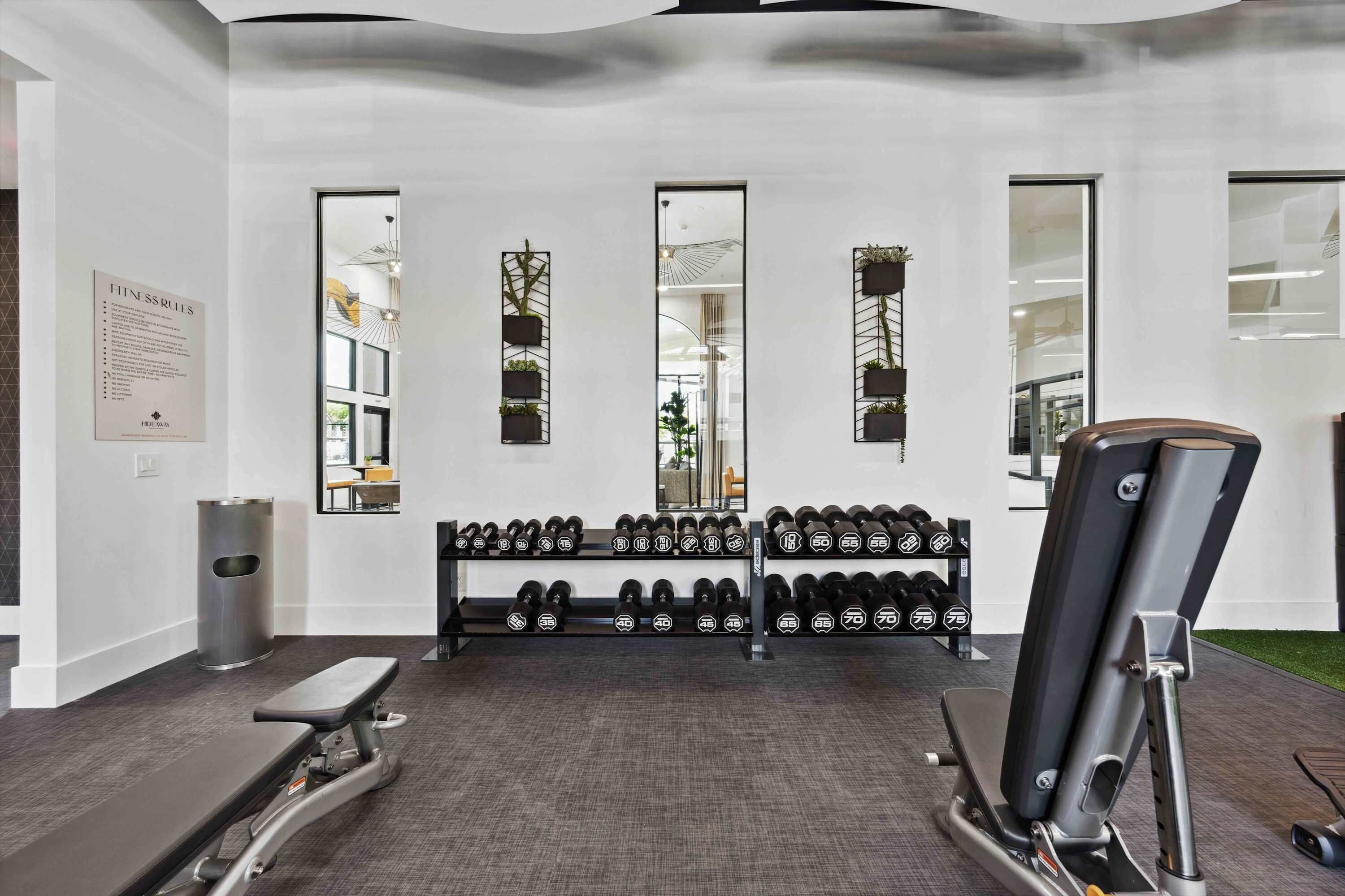Een fitnessruimte met trainingsapparatuur, waaronder gewichten en een bankdrukapparaat.