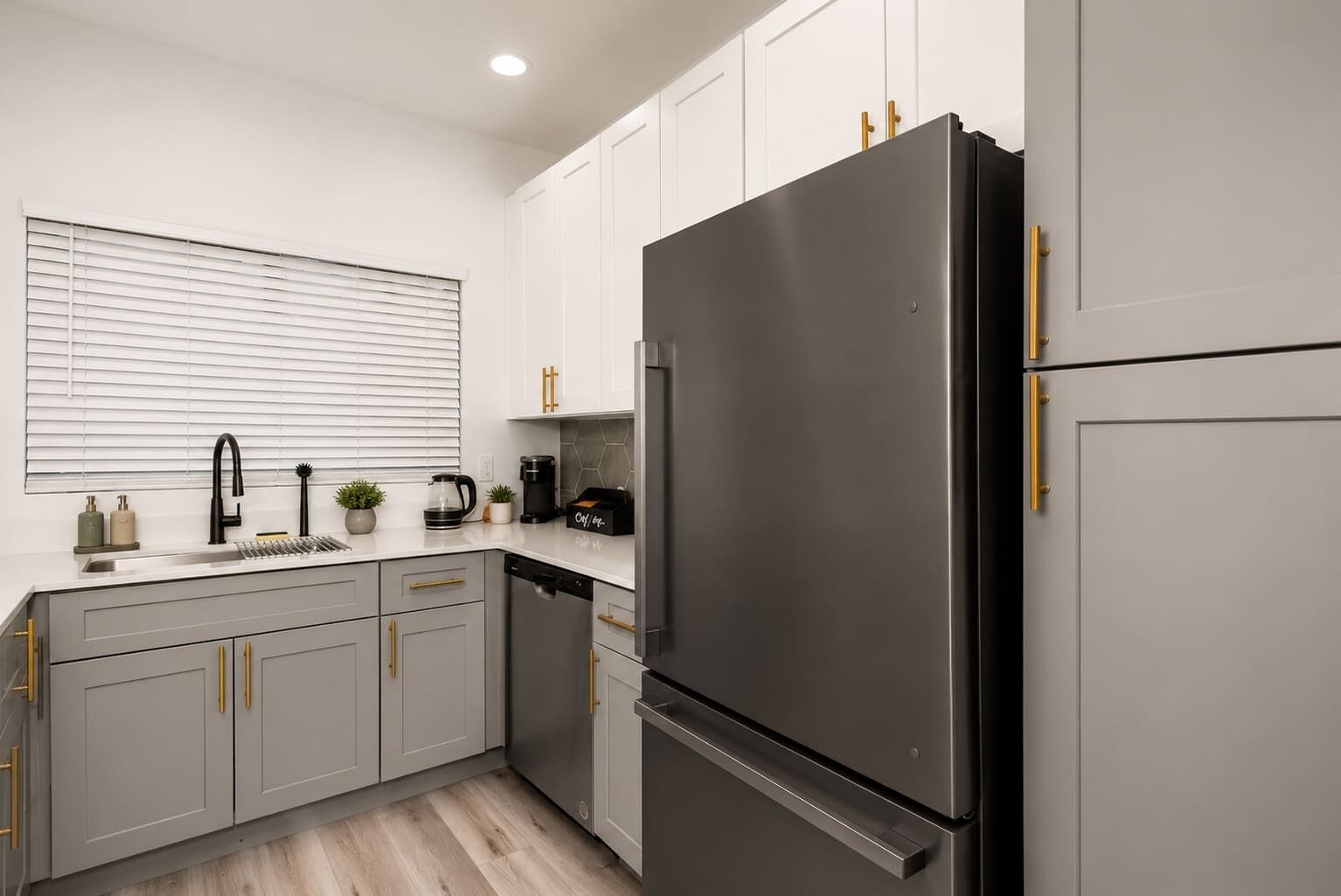 Eine moderne Küche mit einem großen Edelstahl-Kühlschrank, weißen Schränken und goldenen Griffen.