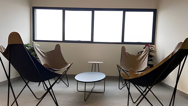 A room with three lounge chairs, a small round table, and a large window with blinds. - Studio com sacada próximo à Paulista (São Paulo)