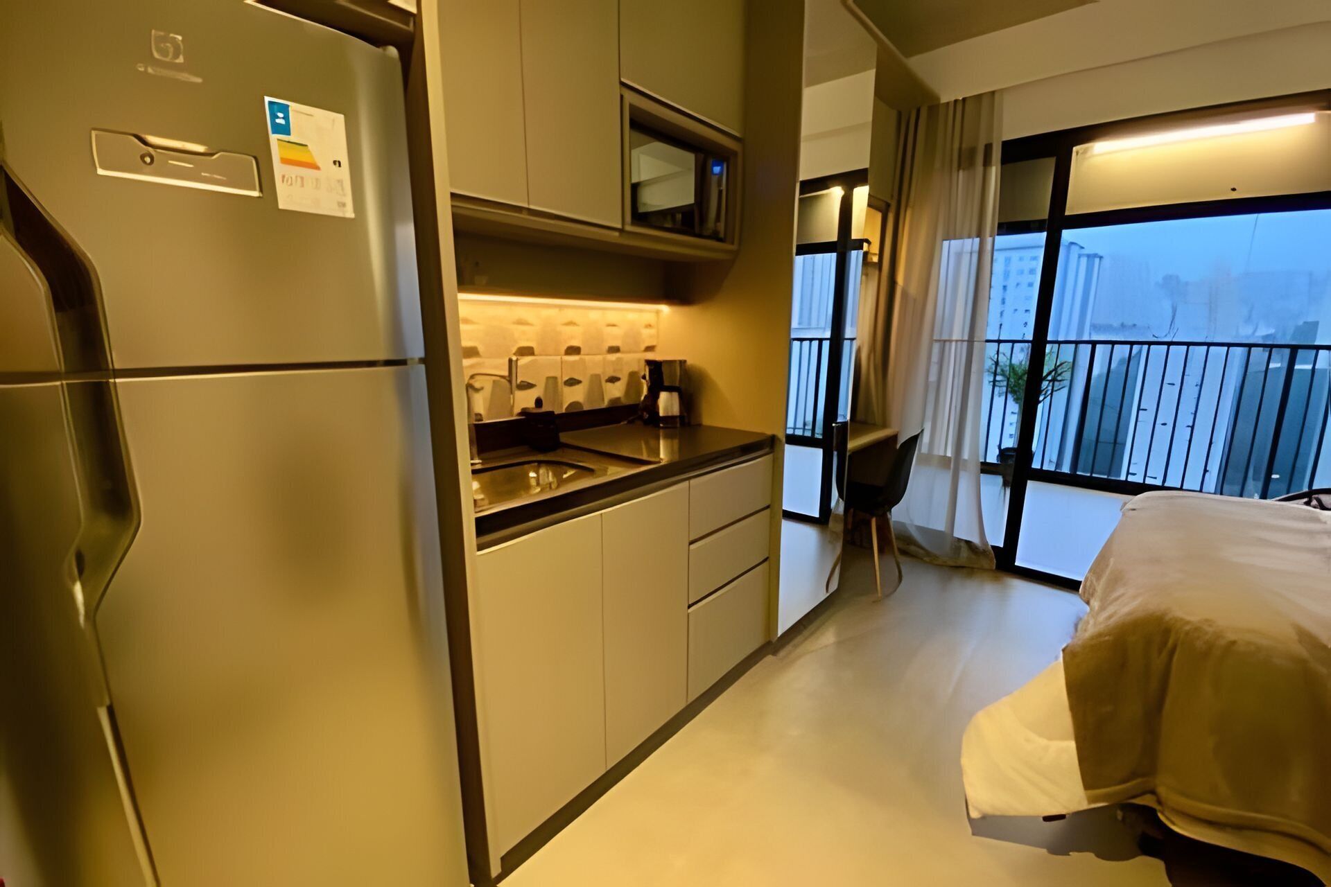 Une chambre d’hôtel compacte comprenant un coin cuisine, un lit et un balcon avec vue sur la ville.