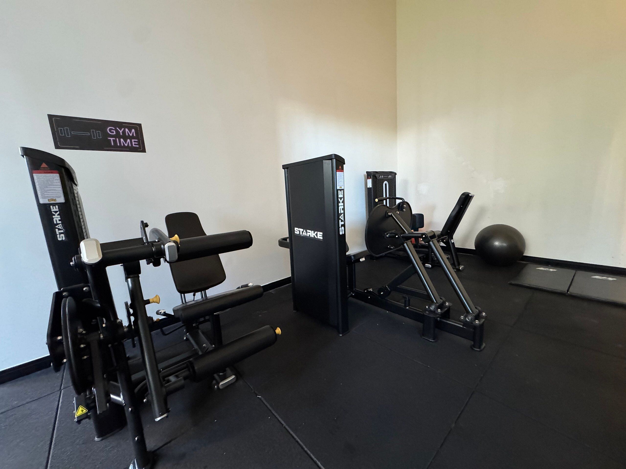 A gym with exercise equipment, a bench, and a wall sign that says "GYM TIME".