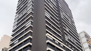 A modern high-rise building with multiple balconies and a green sign indicating a hotel. - Studio com sacada próximo à Paulista (São Paulo)