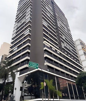 Ein modernes Hochhaus mit mehreren Balkonen und einem grünen Schild, das ein Hotel anzeigt.