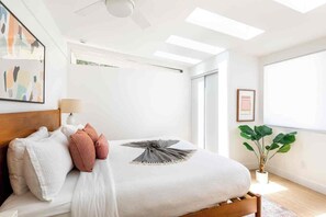 A modern bedroom with a bed, pillows, a lamp, a ceiling fan, and a large window. - Adorable 4-bedroom house in La Quinta with private pool and mountain views! (La Quinta)