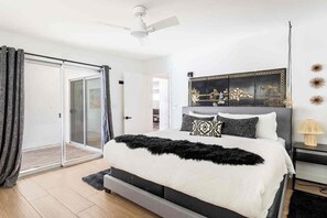 A bedroom with a bed, a sliding glass door, a ceiling fan, and a nightstand with a lamp. - Adorable 4-bedroom house in La Quinta with private pool and mountain views! (La Quinta)