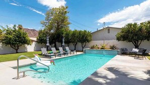 Una piscina con lettini e ombrelloni, circondata da alberi e un edificio.